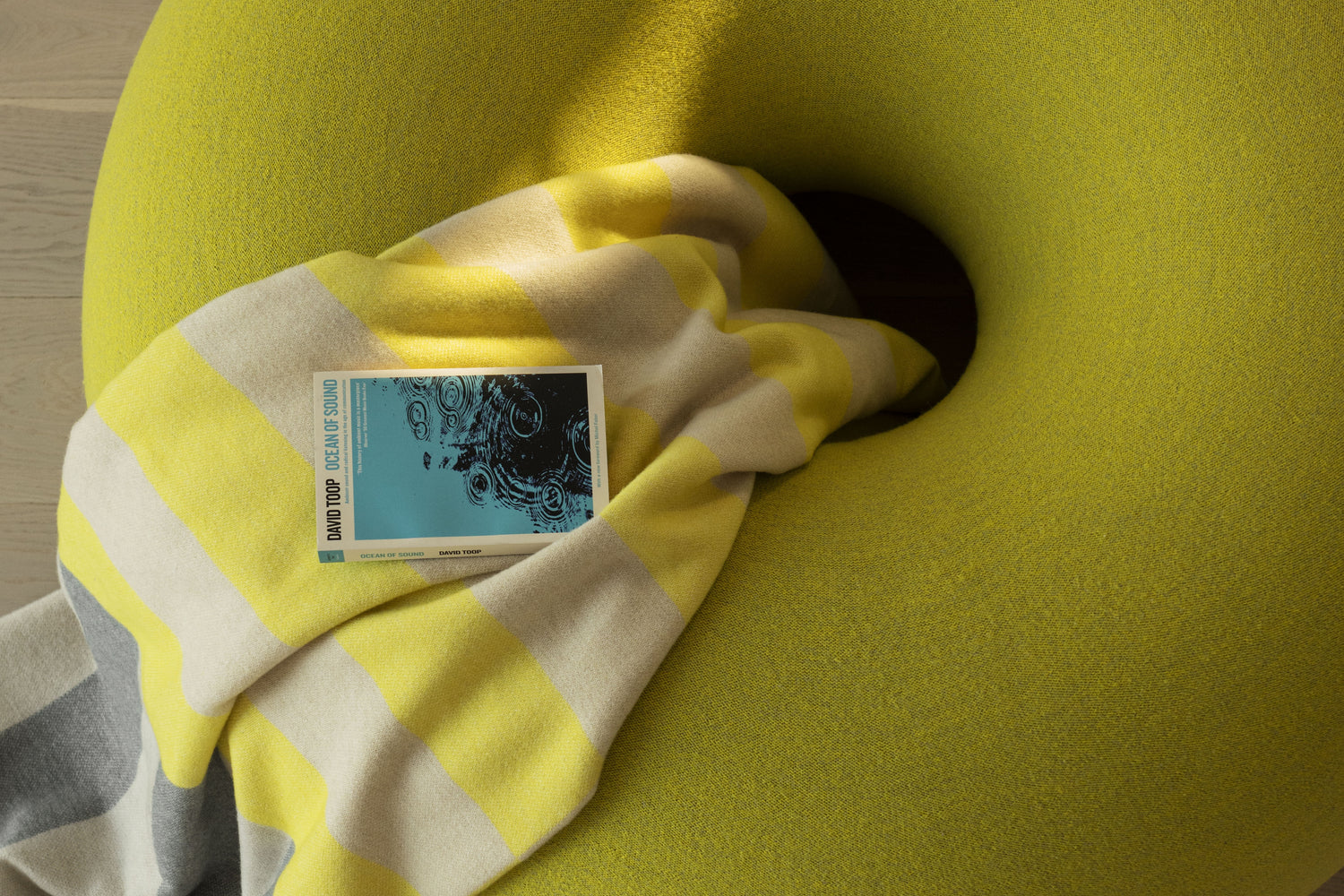 Boa Pouf in Sulfur Yellow with a Yellow / Gray Stripe Throw placed on top. 