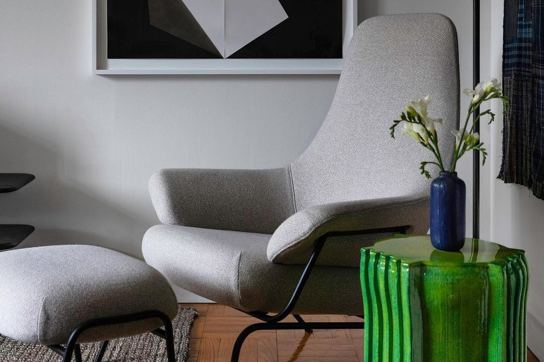 Hai Lounge Chair + Ottoman in Shell / Black PC Metal beside a pedestal with a vase and flower.